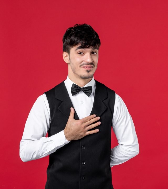 front-view-smiling-male-waiter-uniform-with-bowtie-neck-thanking-someone-red-wall front-view-smiling-male-waiter-uniform-with-bowtie-neck-thanking-someone-red-wall
