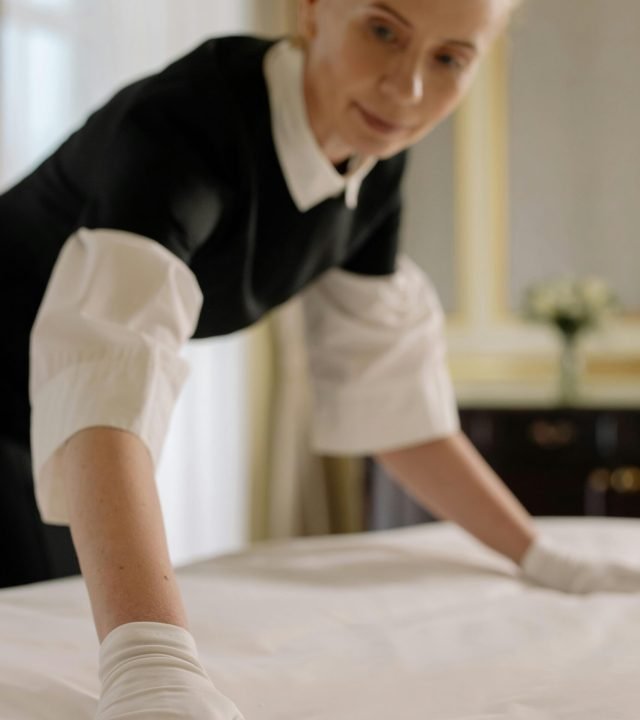 A housekeeper elegantly arranges bed sheets in a luxurious hotel room, showcasing hospitality expertise.