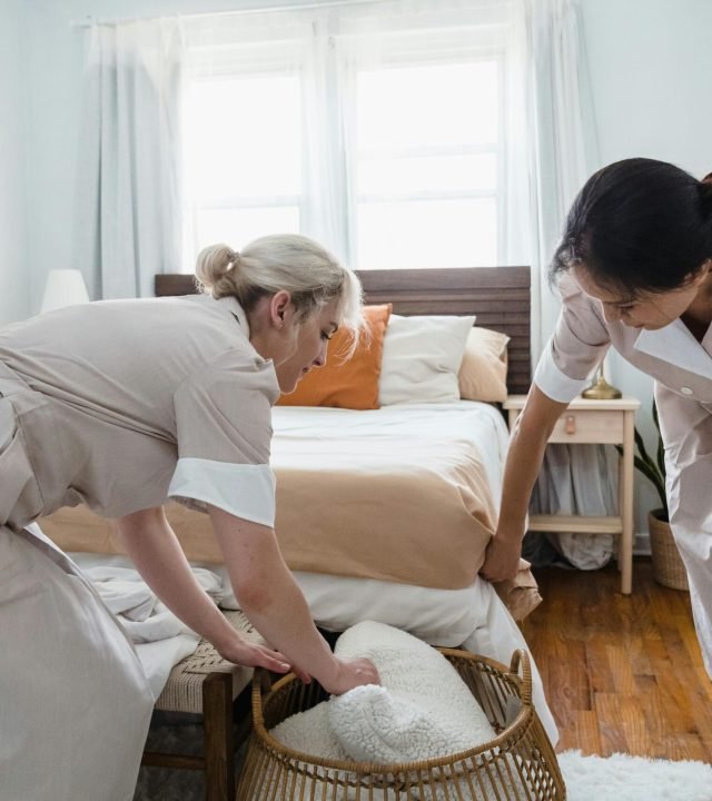 Two housekeepers organizing a bedroom, focusing on tidiness and comfort.